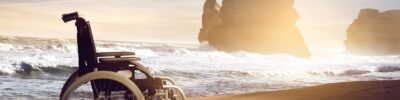 Ein leerer Rollstuhl vor einem Meer mit Wellen.